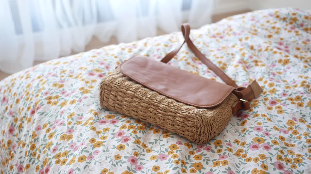 Borsa a tracolla di paglia marrone su biancheria da letto floreale