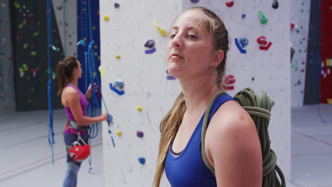 뒷면에 로프를 고 있는 백인 여성의 초상화. 실내 등반 벽에서 카메라로 돌아가고 있다.