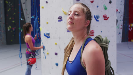 Porträt-Einer-Kaukasischen-Frau-Mit-Seil-Auf-Dem-Rücken,-Die-Sich-An-Einer-Indoor-Kletterwand-In-Die-Kamera-Dreht