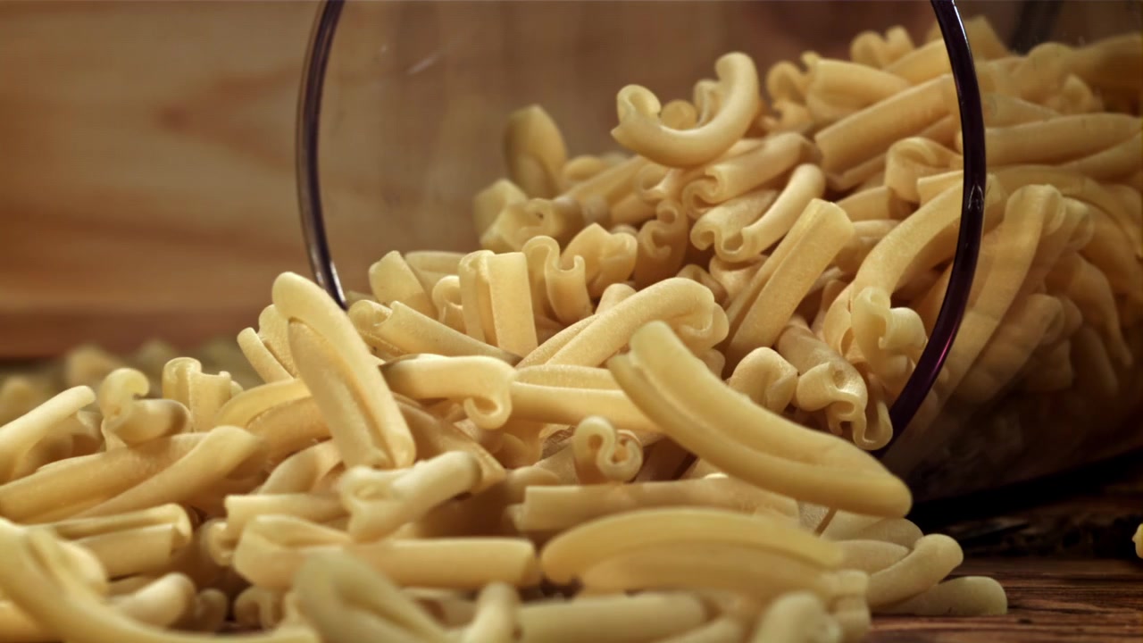 Pasta secca versata da una ciotola di vetro su un tavolo di legno rustico