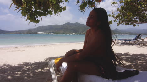 latin girl sat in shade on tropical white sandy beach gets up to swim in ocean water, playa teco maimon