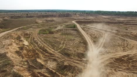 vista aérea de una cantera de arena con huellas de neumáticos y bosque en el fondo