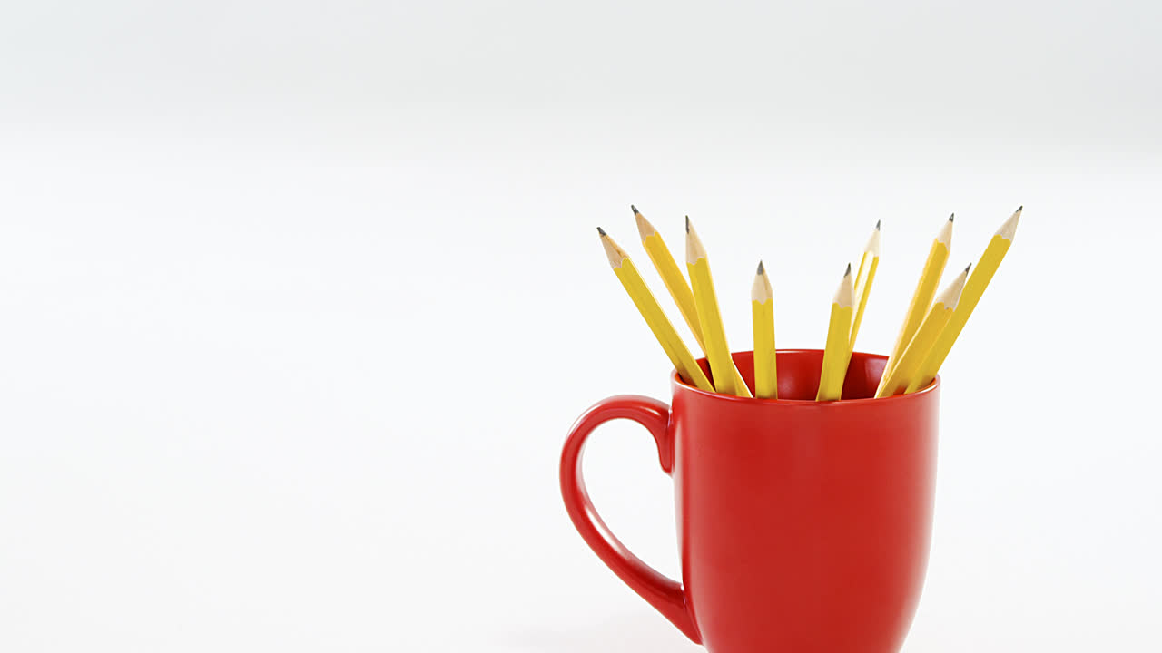 lápices de color amarillo guardados en taza roja sobre fondo blanco