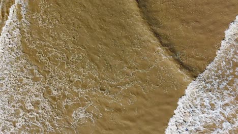 aerial footage of waves gently breaking on the beach, with golden sand