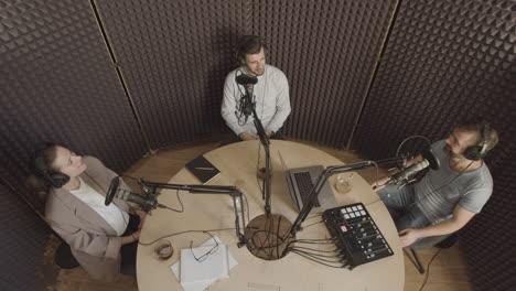 overhead general shot of three people having a funny conversation in a radio recording studio