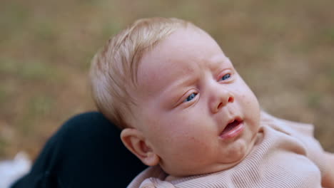 cute serious infant with blonde hair. kid lies on mom's knees and her hands hold baby's cheeks. close up.