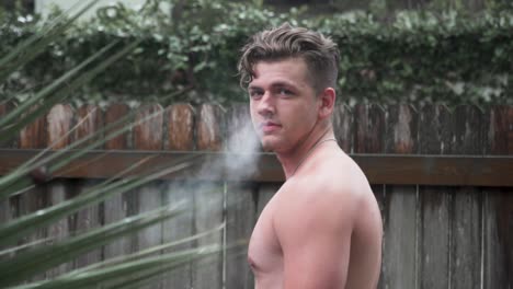 modelo masculino mirando hacia atrás a la cámara soplando humo a cámara lenta