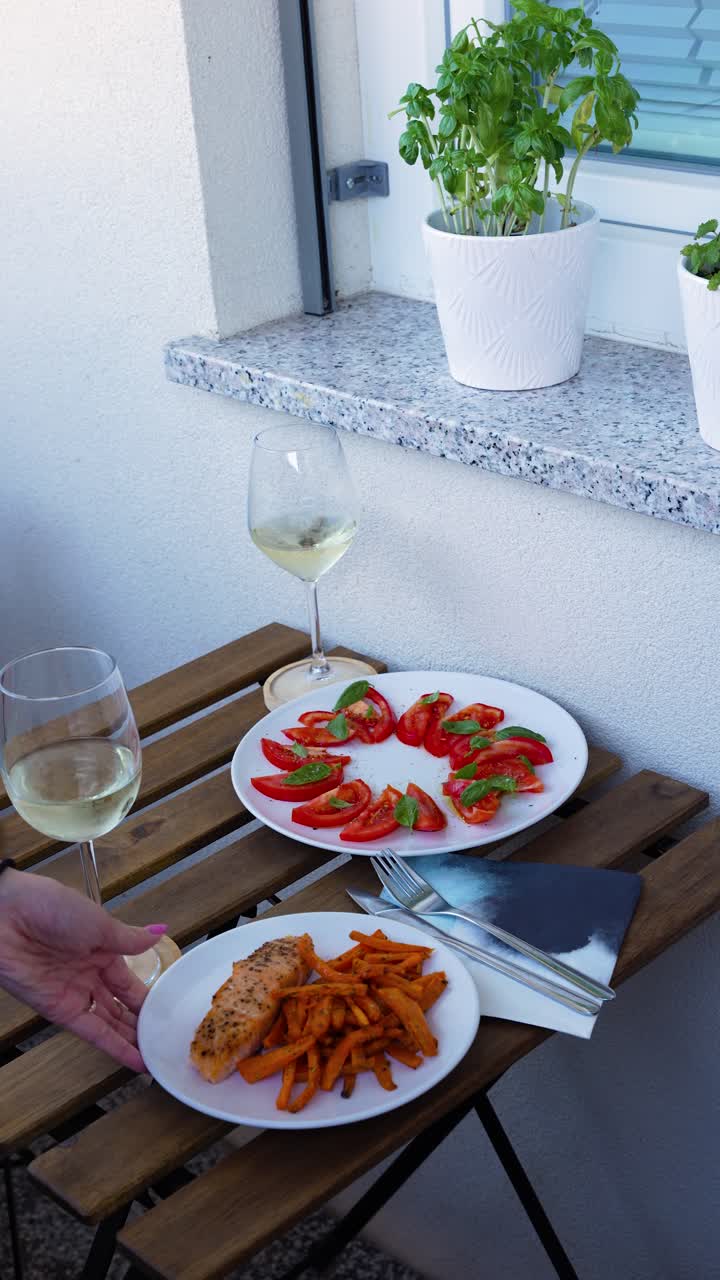 Due bicchieri di vino bianco, un piatto di insalata di pomodori e basilico e un piatto di salmone con patatine fritte su un tavolo di legno. Scatto verticale