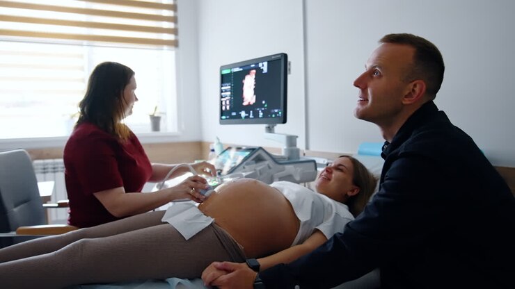 Happy smiling lady expecting a baby are at doctor's. Woman is having the ultrasound check up in hospital.