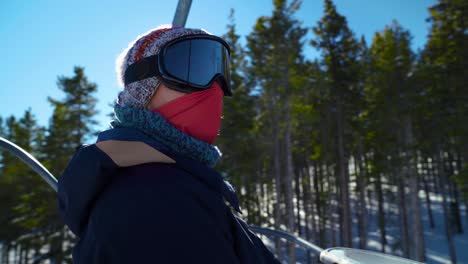 woman skier with face mask rises up on a ski lift in mountain resort