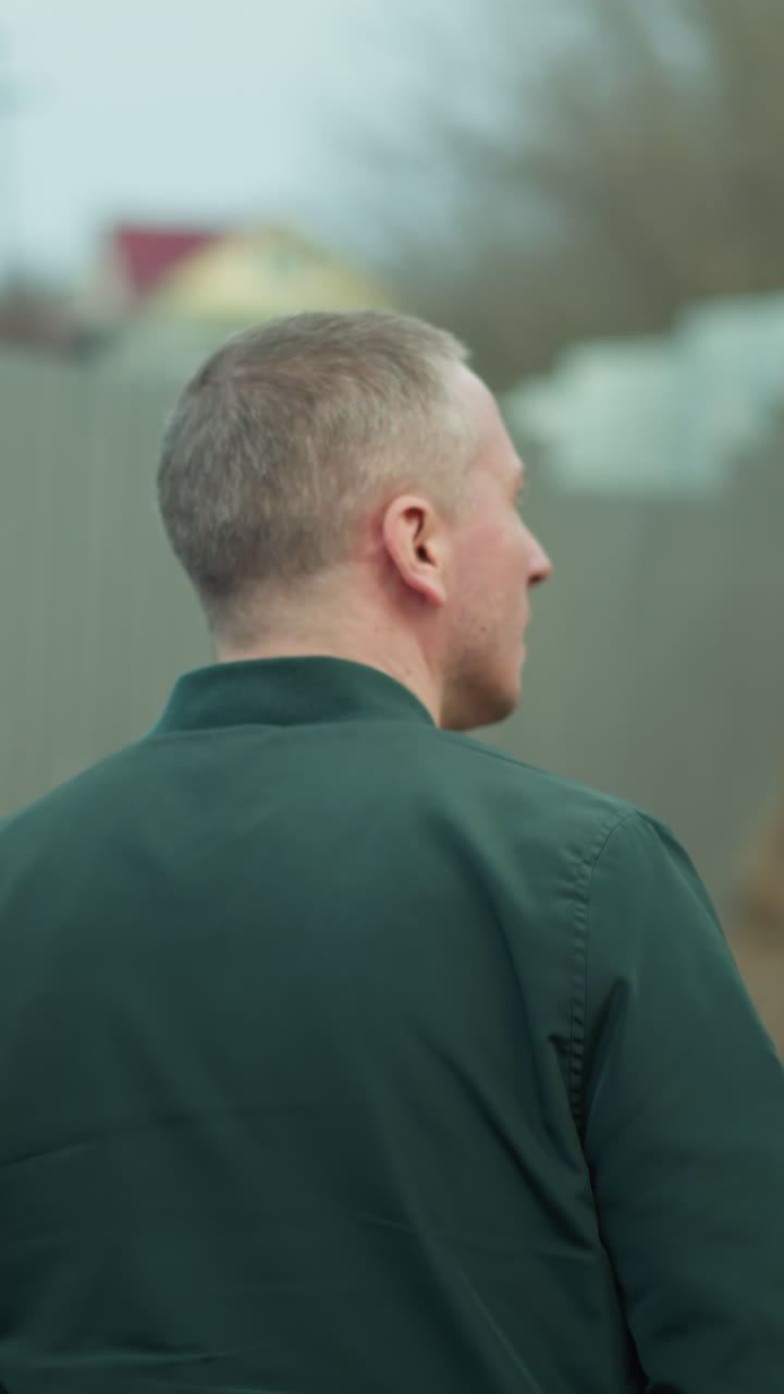 울타리를 따라 걸어가는 남자의 가까운 시선, 뒤에서 찍은, 그의 머리와 재의 뒤쪽의 시선, 산업 지역의 흐릿한 배경과 함께