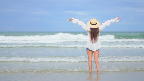 back view of woman with shorts and hat on seashore raising arms