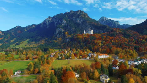 relaxing view of drone flying over village houses towards castle on hill over scenic autumn field in the afternoon near the neuschwanstein castle in germany, europe, wide view