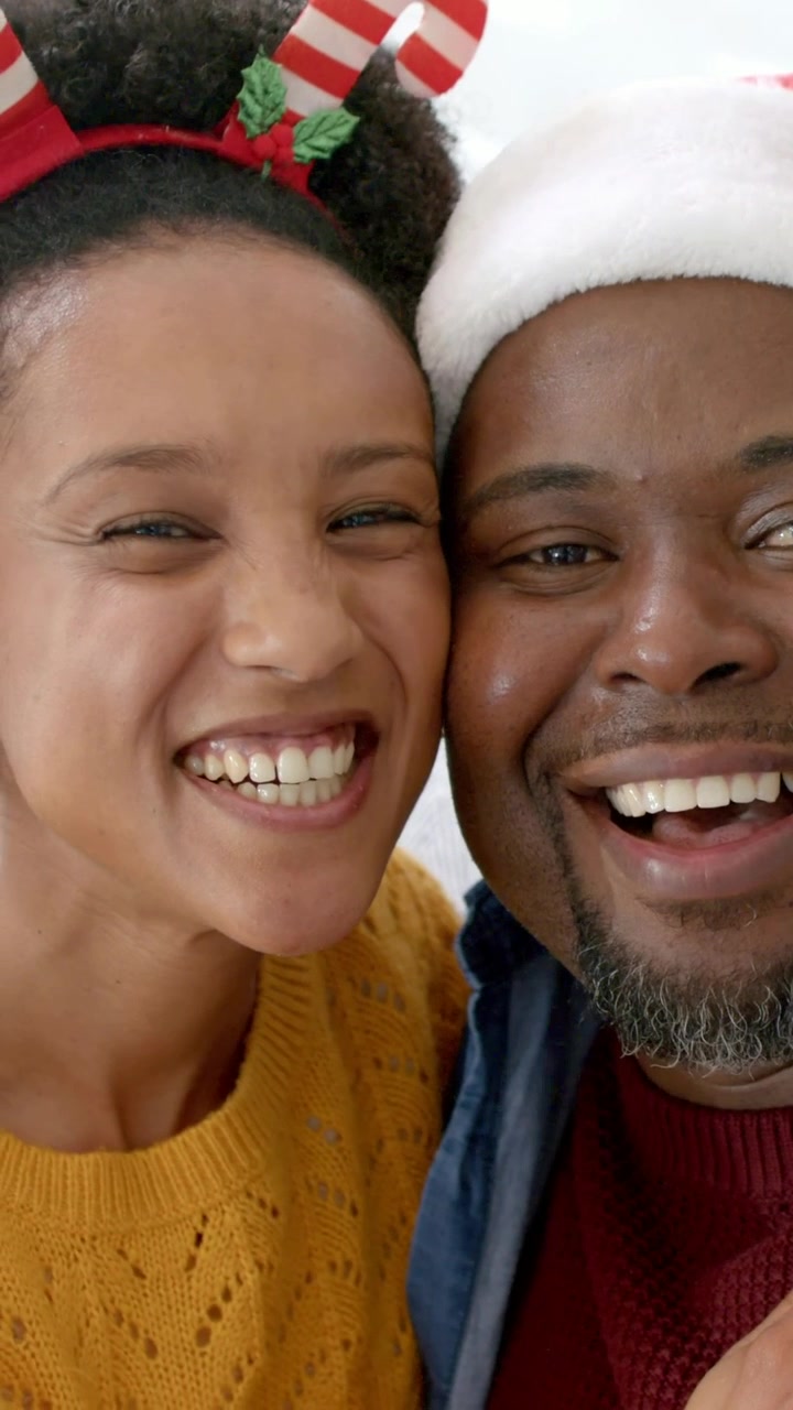 Vertical video: Pressing cheeks, couple smiling and laughing at home for holiday with Santa hat