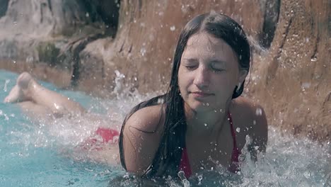 calm girl lies in pool under falling down jets slow motion