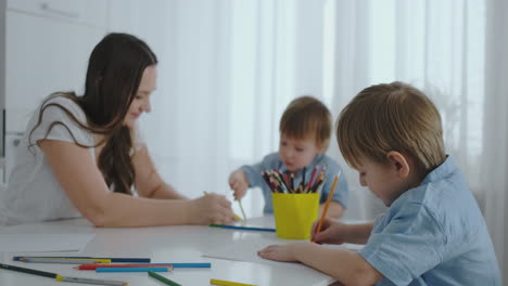 dos niños dibujan con su madre sentada en la cocina. una familia feliz en casa.