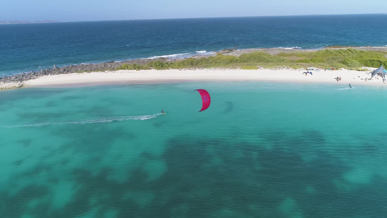 el kitesurfista rojo navega a través de la isla de los crasky rocas atrapando aire sobre el agua azul del océano