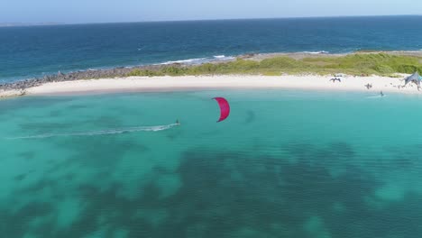 Red-kite-surfer-sails-through-crasky-los-roques-island-catching-air-above-blue-ocean-water