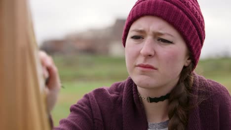 face of young woman painting outside with serious look