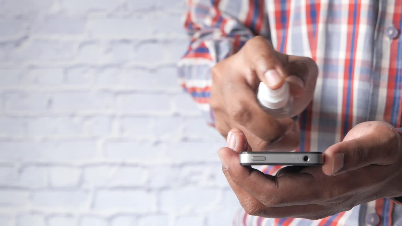 한 남자가 드세니타이저로 드폰을 소독하고 있습니다.