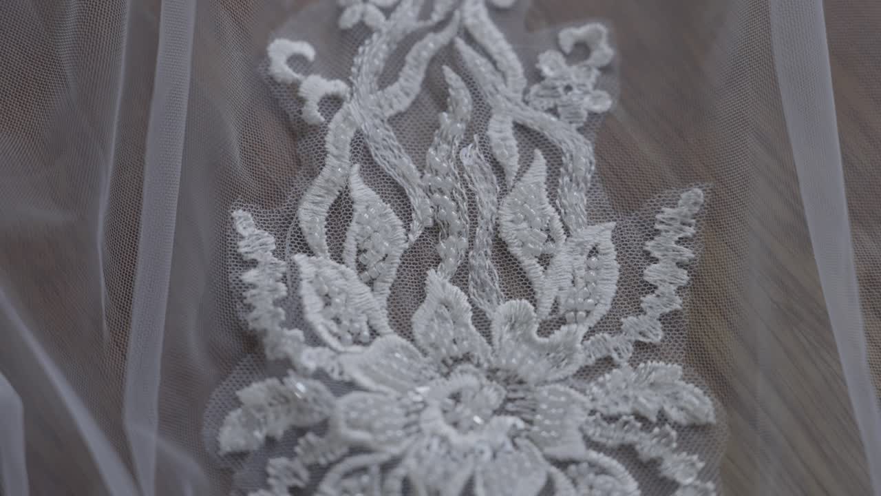 Dettaglio in primissimo piano di intricati ricami floreali in pizzo e delicate perline bianche su un velo da sposa.