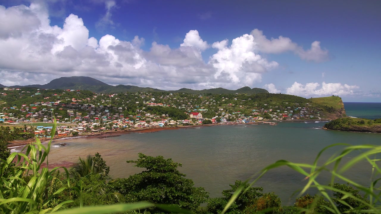 Pemandangan Indah Teluk Dennery dari Titik Mandele di Saint Lucia, Menampilkan Desa Lereng Bukit Berwarna-warni, Pelabuhan Tenang, dan Tebing Hijau Subur yang Bertemu Samudra Atlantik