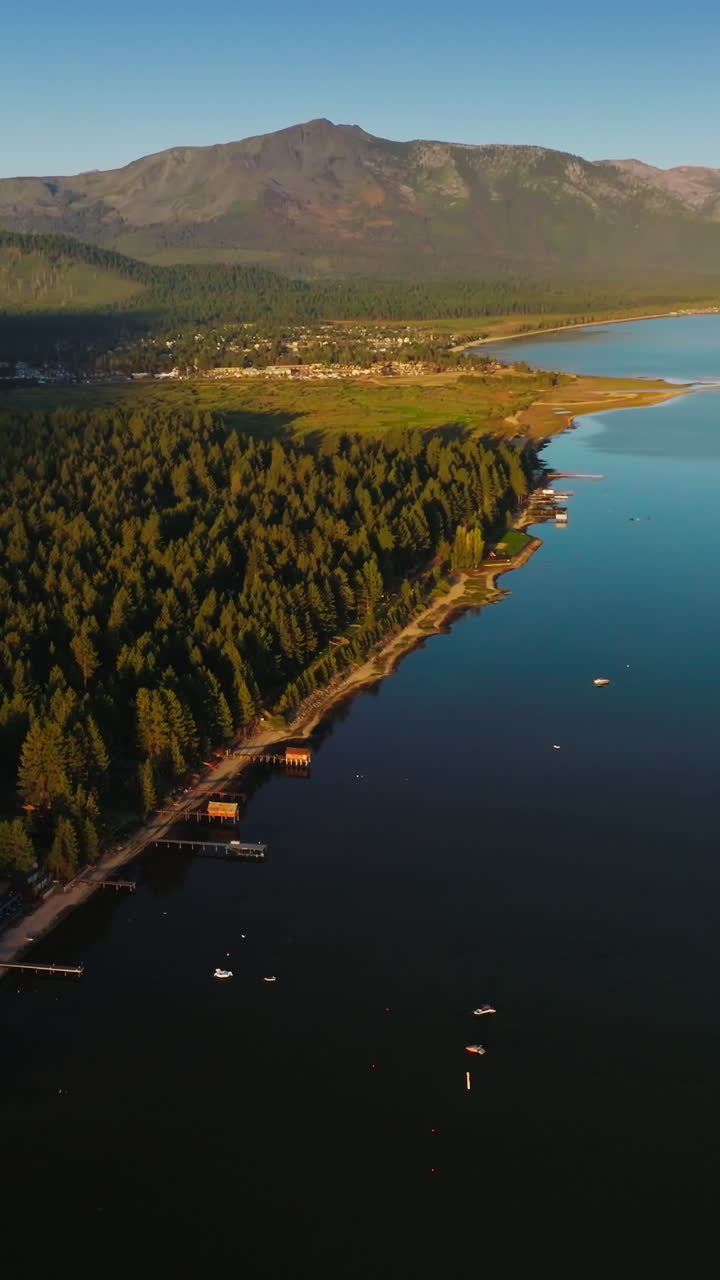 Calm surface of the Lake Tahoe at setting sun. Pine tree forest covering the rocky shore of the lake. Aerial perspective. Vertical video