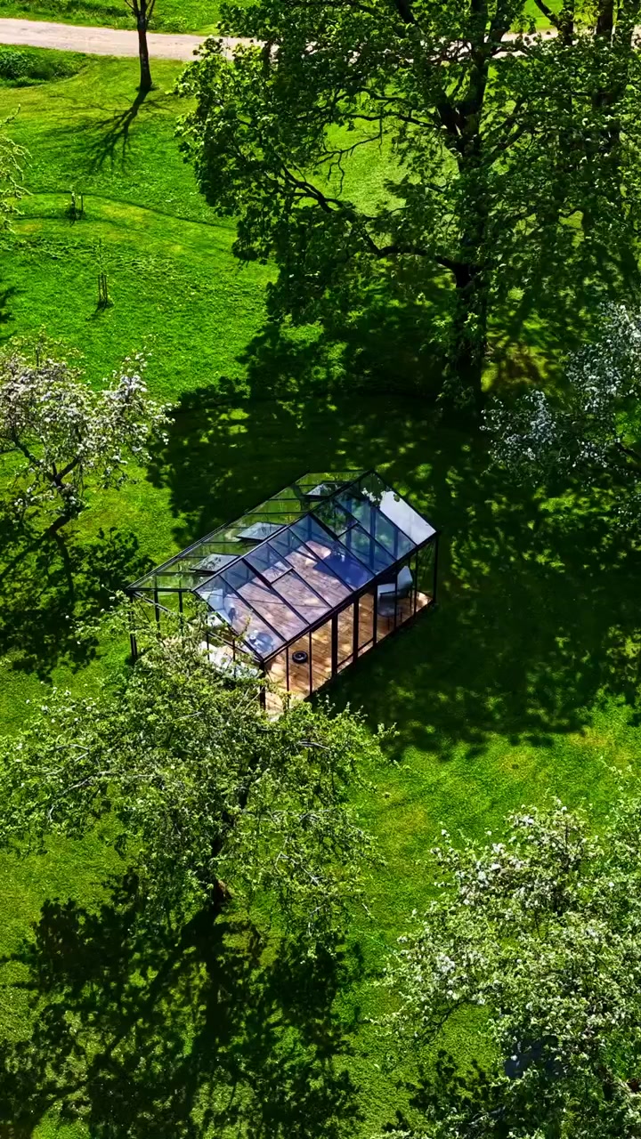 Moderna serra in vetro circondata da alberi verdi ed erba in un giardino rurale. Vista aerea dall'alto, formato verticale.