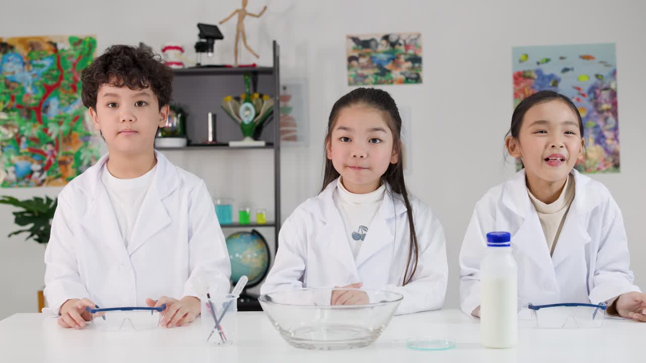 白衣姿で理科の授業のためにテーブルに座っている3人の若いアジア人学生