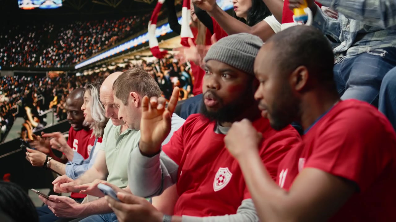 Divers supporters de football utilisant une application de paris sportifs mobile pendant un match de football en direct