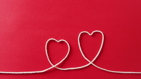 Video-of-close-up-of-hearts-of-string-on-red-background