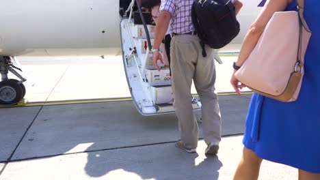 pasajeros que abordan un pequeño avión de cercanías por escalera, personas irreconocibles y disparadas por detrás en la pista del aeropuerto