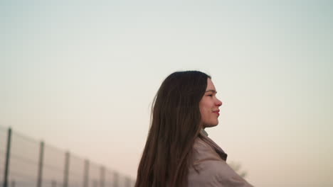 a close-up view of a young woman in a peach jacket, enjoying a moment of rollerblading with a joyful expression on her face. the background features a soft, pastel sky at sunset