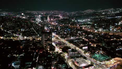 flying over mexico city lit up at night with mixcoac downtown cityscape skyline, aerial