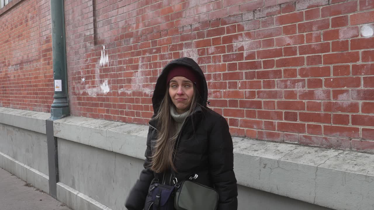 Portrait wide shot of caucasian female standing in front of a brick wall while talking in winter clothing.