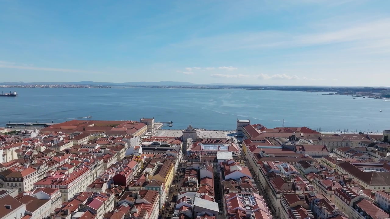 Lenta panoramica con drone di Praça do Comércio e Arco di Rua Augusta, Lisbona a mezzogiorno. Cielo azzurro limpido, fiume Tago in lontananza.