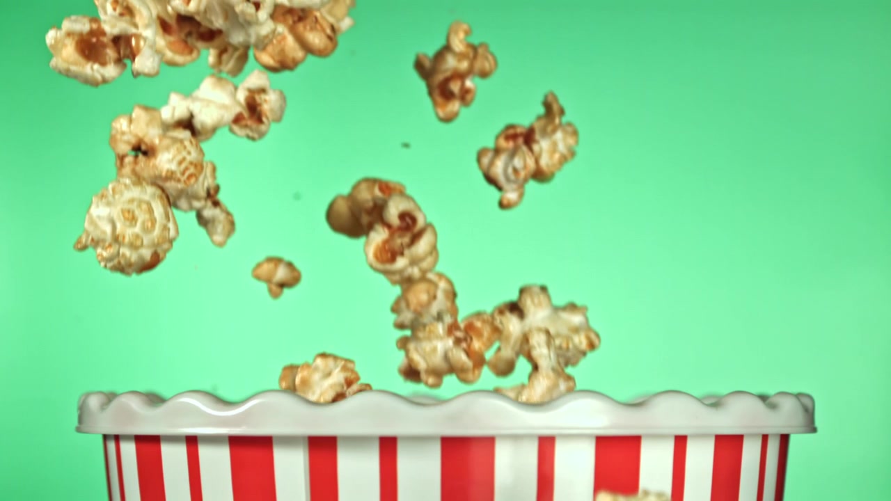 Popcorn al rallentatore che cadono in un secchiello a strisce rosse e bianche