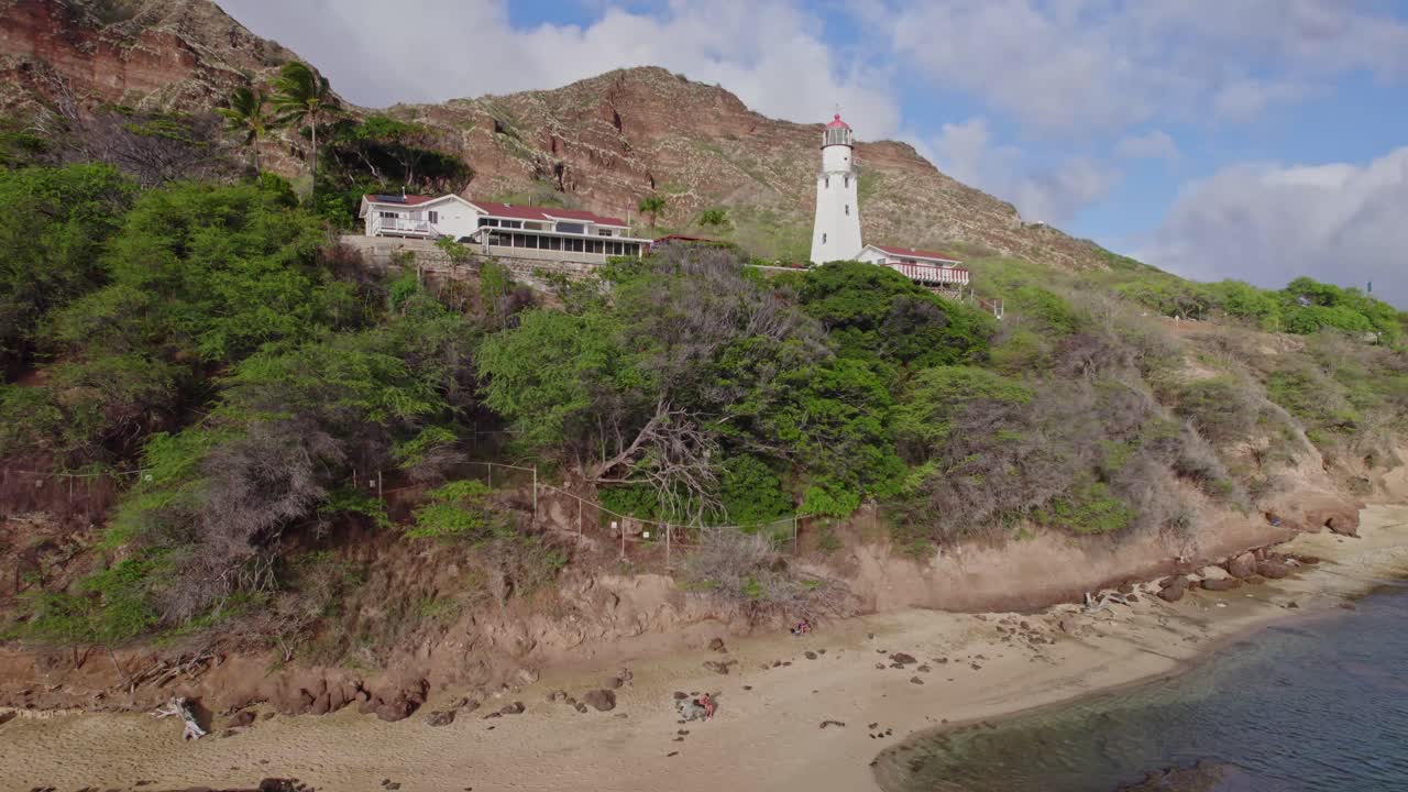 imágenes de drones del faro de diamond head retrocediendo para revelar la playa de arena y el agua azul del pacífico que se encuentran debajo