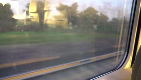 industrial area with trees and big building from a train window, with reflection of sunset