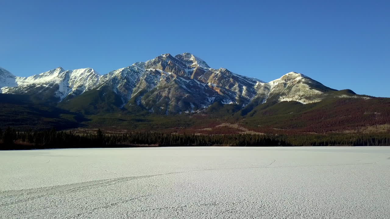 Volo di drone sopra un lago ghiacciato verso una montagna coperta di neve a Jasper, Canada.
