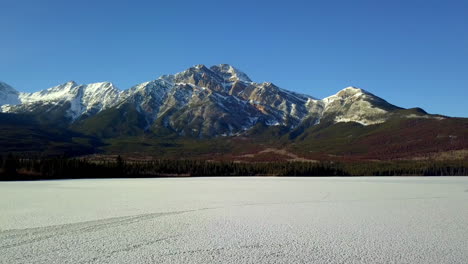 drone flight over a frozen lake towards a snow covered mountain in jasper, canada