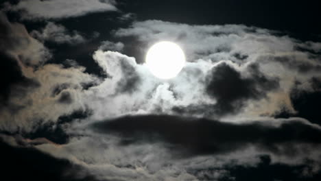 a bright full moon rises as clouds move quickly in a night sky