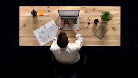 joven está trabajando en la computadora portátil, observa el plan del edificio, durante el día, concepto de trabajo, concepto de oficina, concepto de comunicación, top shot