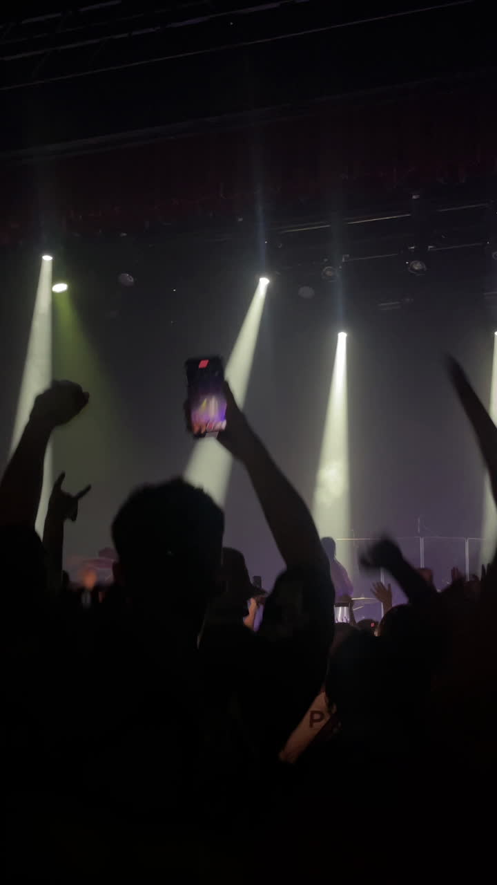 Multitud de asistentes a un concierto con las manos levantadas disfrutando de música en vivo bajo luces de escenario vibrantes