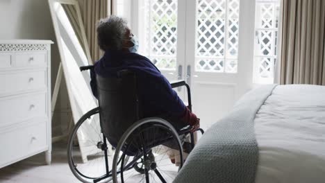 senior african american woman wearing face mask sitting on the wheelchair at home