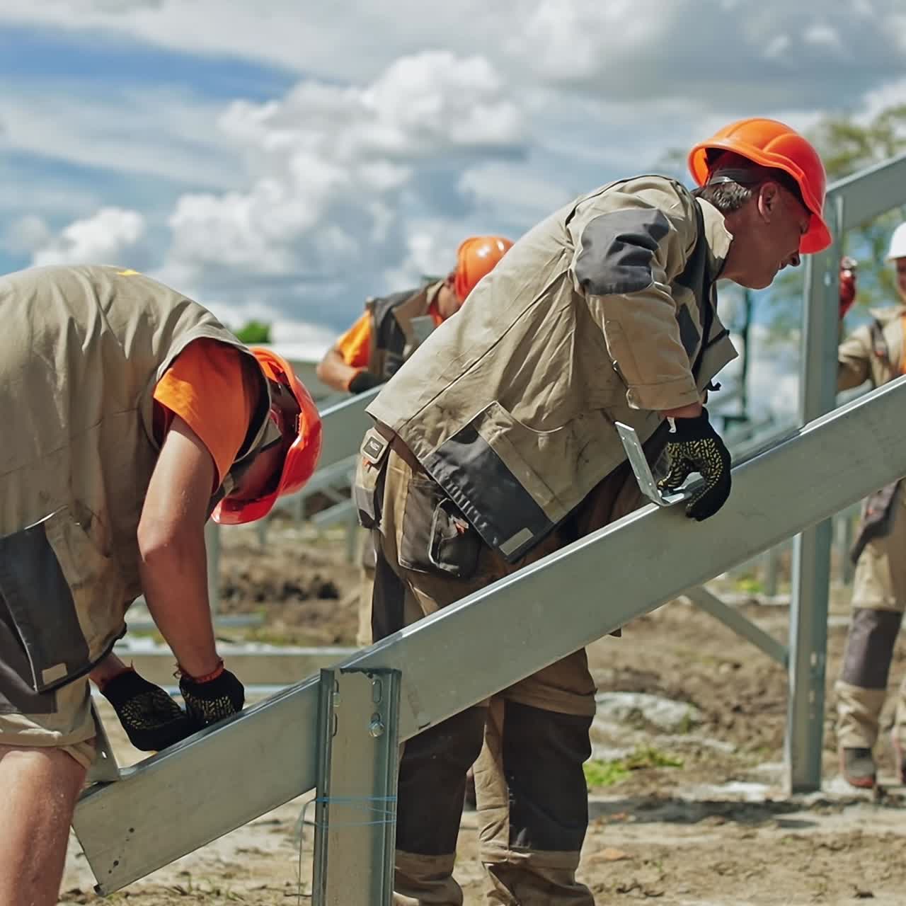 Solar technicians build metal base for solar panels. Workers in uniform and safety helmets construction new solar farm on a field.
