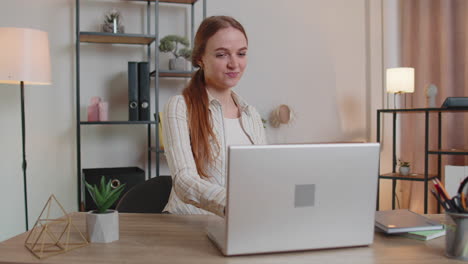 caucasian young woman sitting at table opening laptop pc starting work online in room at home office