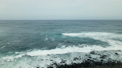 ocean waves splash on rocky coast of maui island, surfers waiting for wave