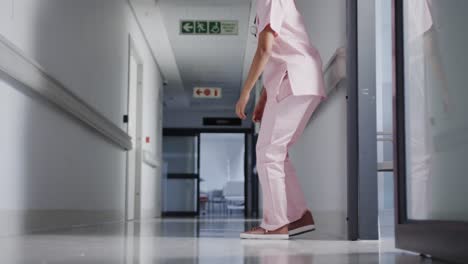 stressed biracial female nurse leaning on wall in hospital in slow motion