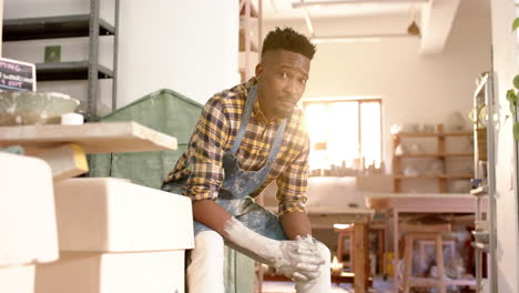 happy african american male potter resting and smiling in pottery studio, slow motion